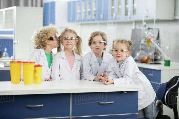 Four kids in science laboratory wearing coats and standing at table ...