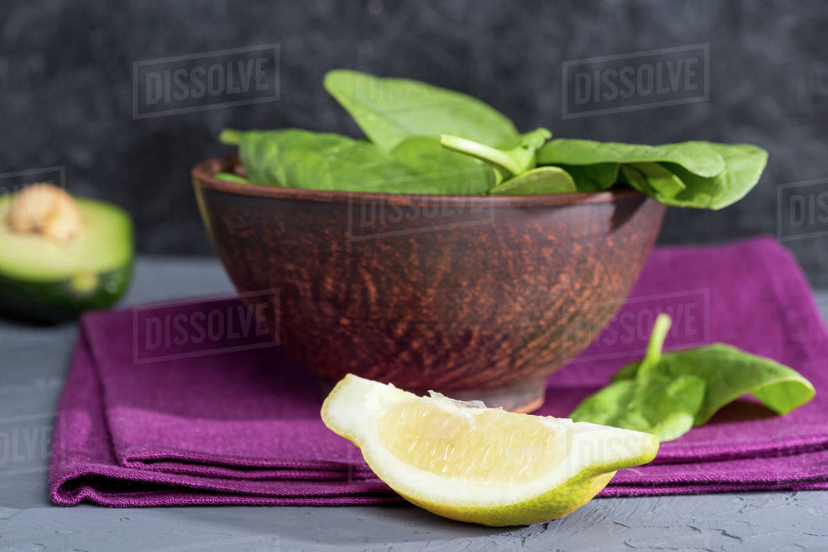 Bowl of fresh spinach on linen with piece of lemon on tabletop Stock