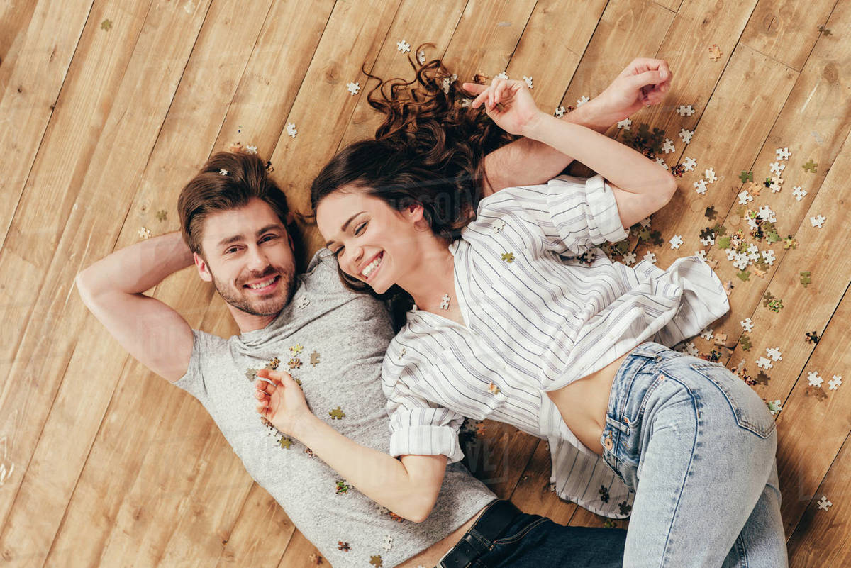 Above view of young smiling couple lying on wooden floor at home