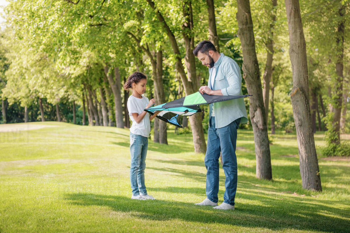 Side view of father and little daughter assembling kite together