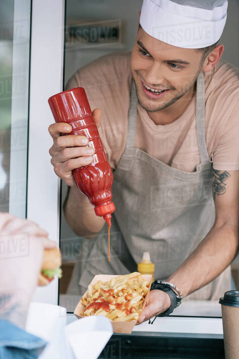 Smiling chef adding ketchup to hot dog in food truck Stock Photo