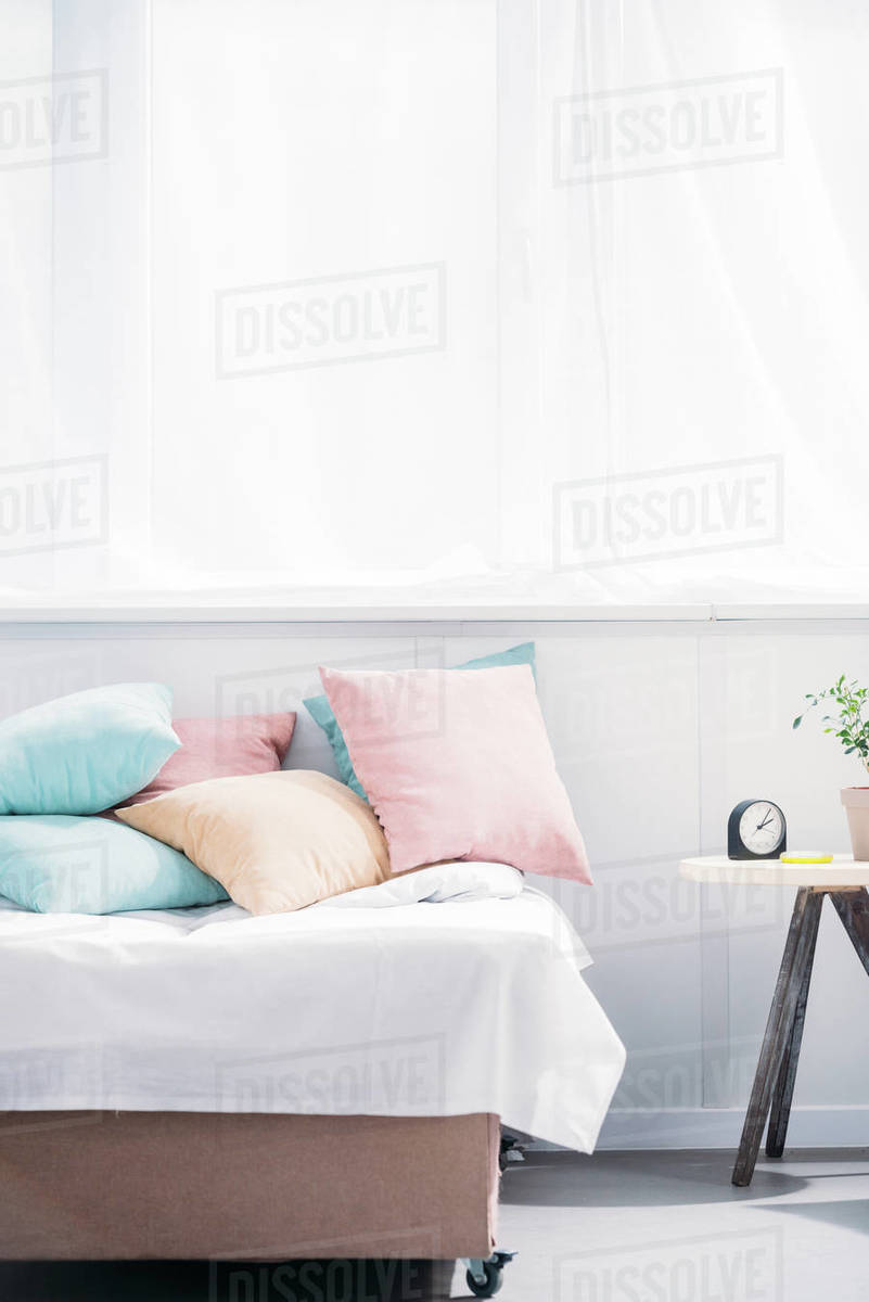 Bed With Lot Of Pillows In Modern Light Room With Alarm Clock And