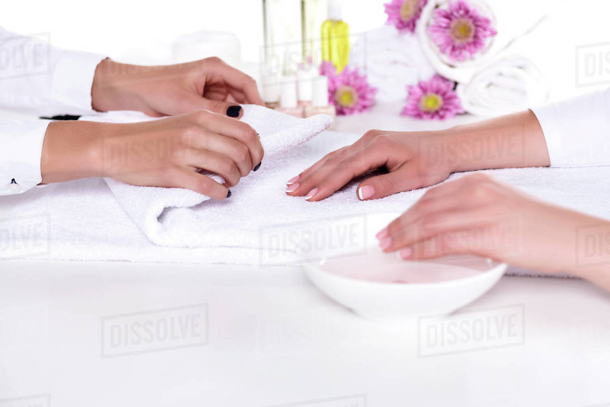 Cropped image of manicurist rolling towel to dry hand of woman while