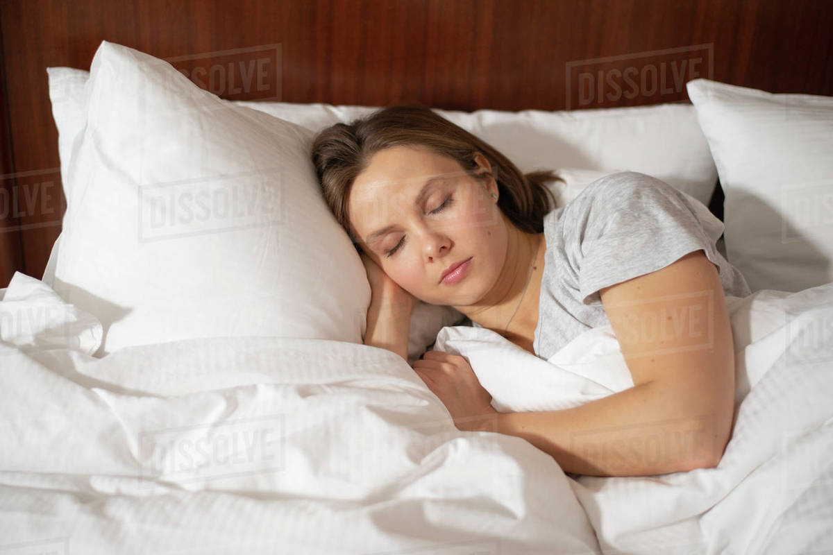 Woman cozily sleeping in bed putting her hand under head Stock Photo