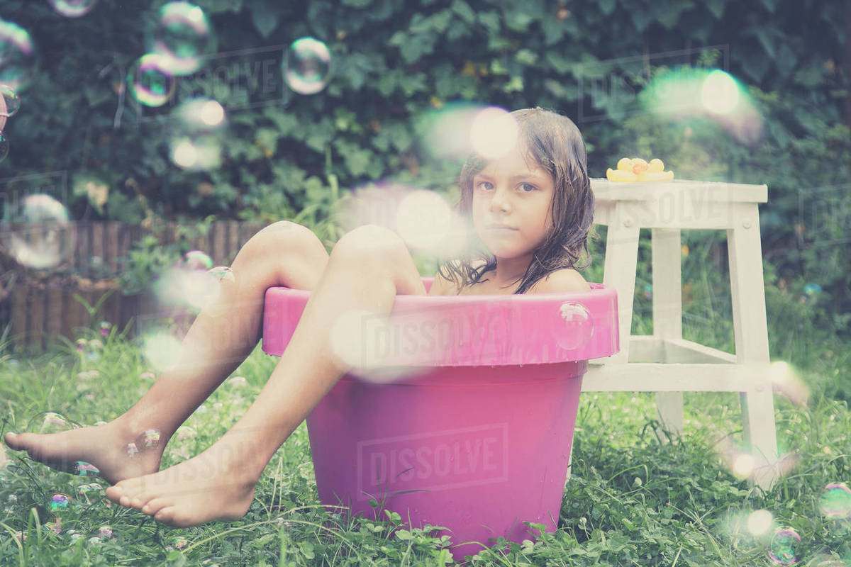 Boy sitting in a bucket of cold water cooling off in summer heat with