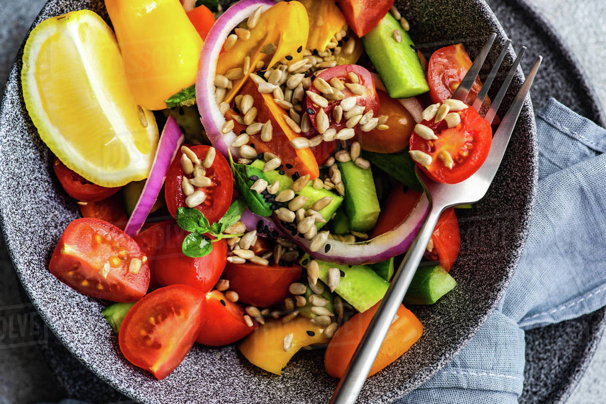 Bowl of tomato, cucumber, red onion and pepper salad with fresh sunflower seeds and lemon