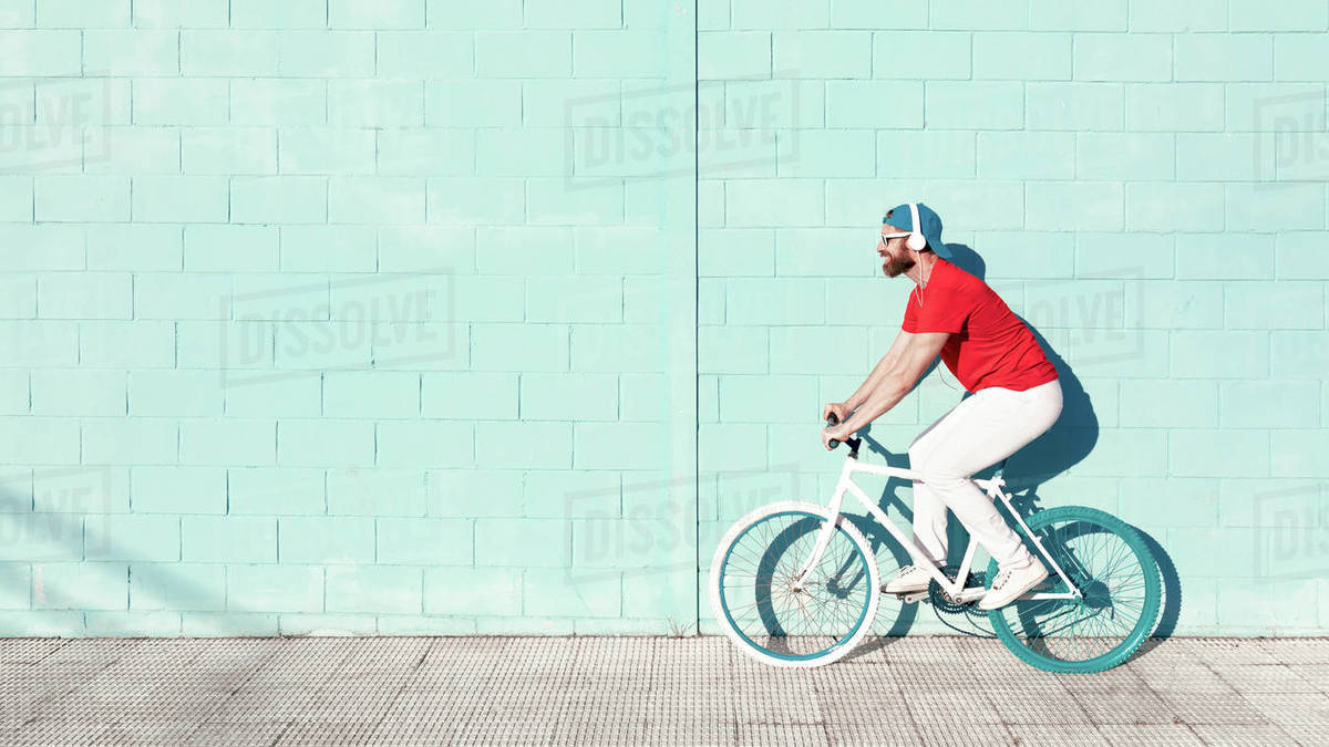 Side view of young active bearded male cyclist in stylish outfit