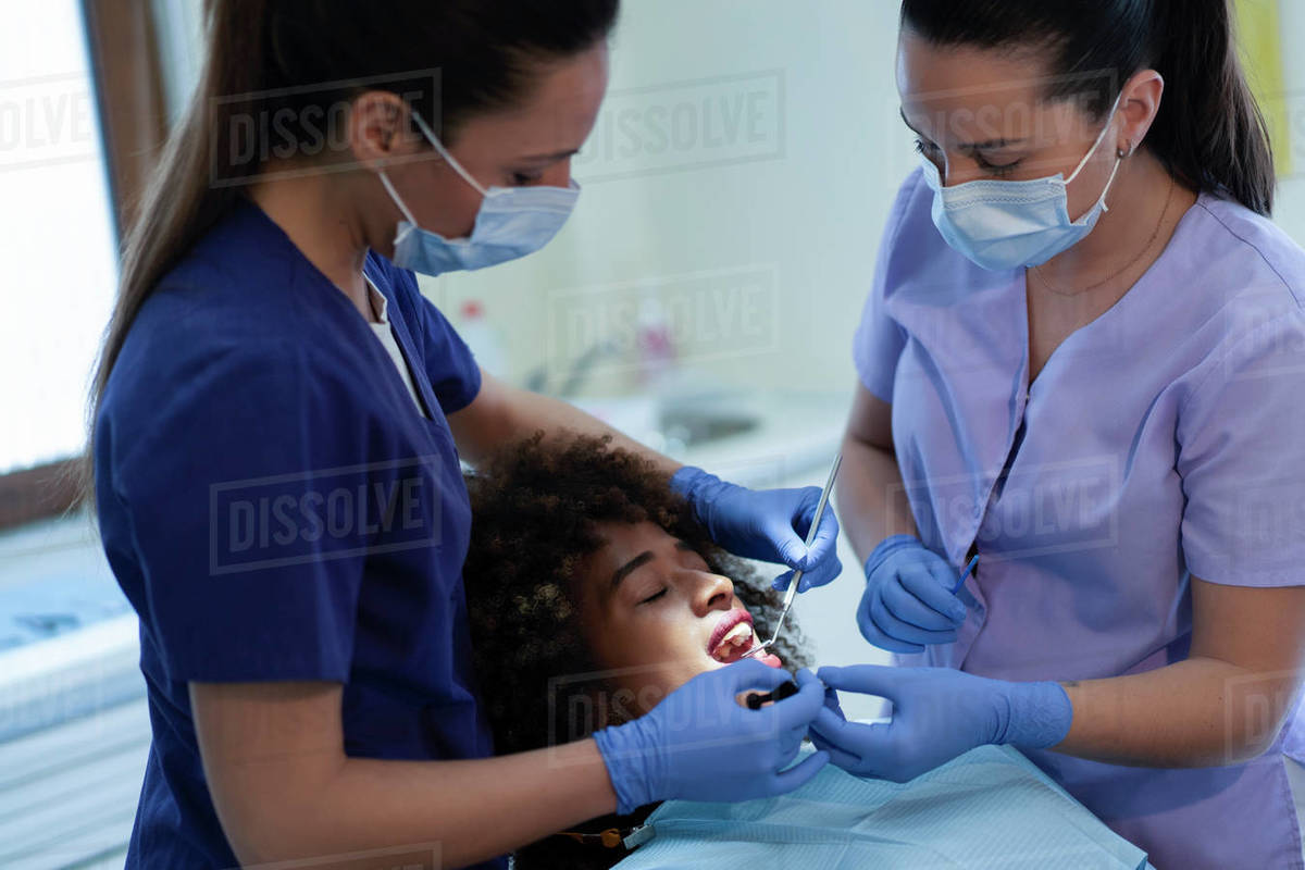 Female assistant holding suction device while dentist using mirror and