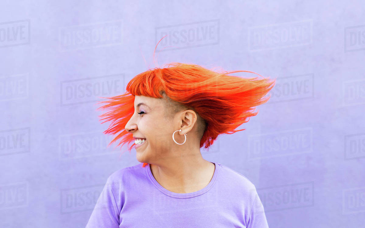 Excited adult female with closed eyes shaking bright ginger dyed hair