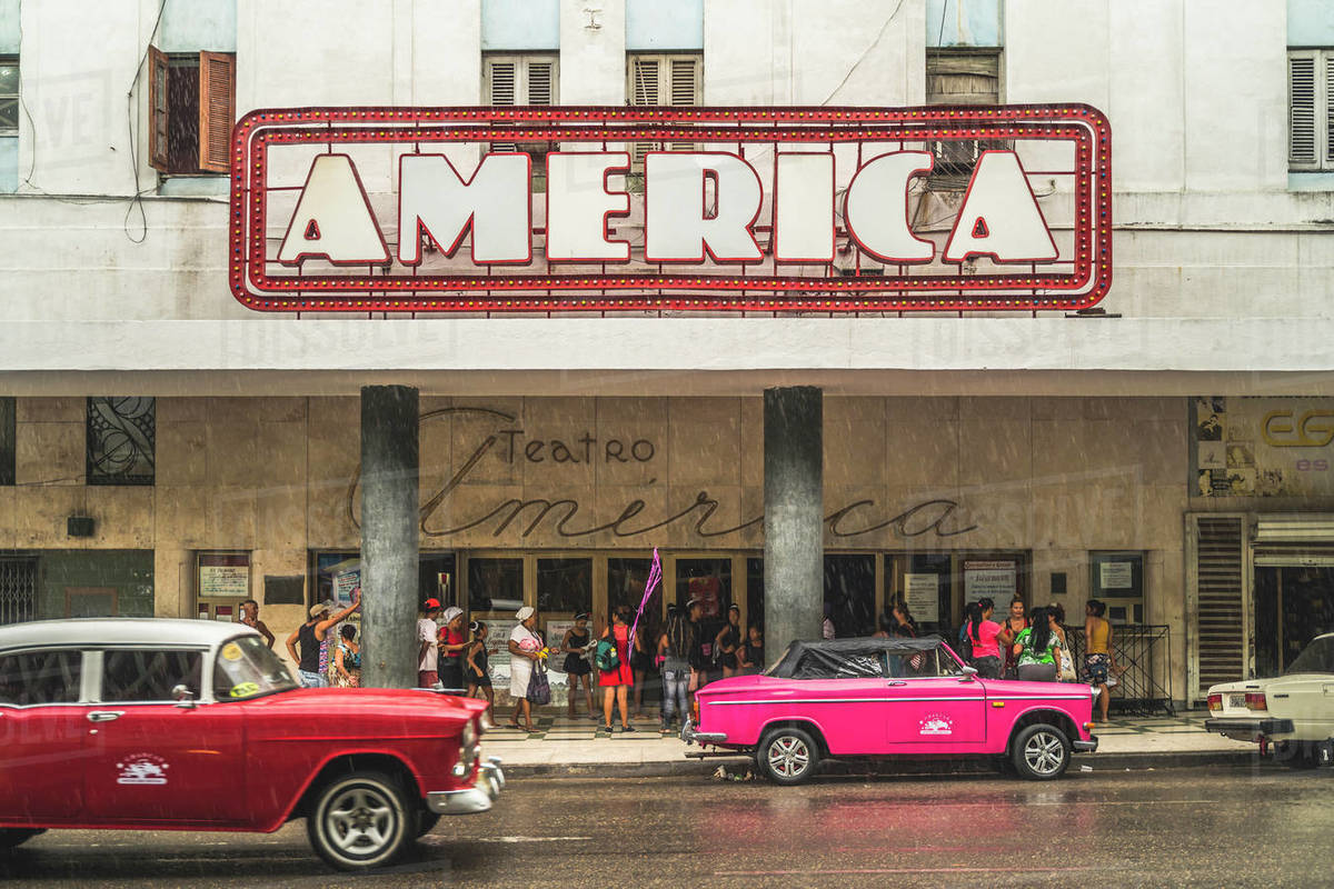 Pink and red vintage cars outside Teatro America in rain, La Habana (Havana), Cuba, West Indies, Caribbean, Central America Royalty-free stock photo