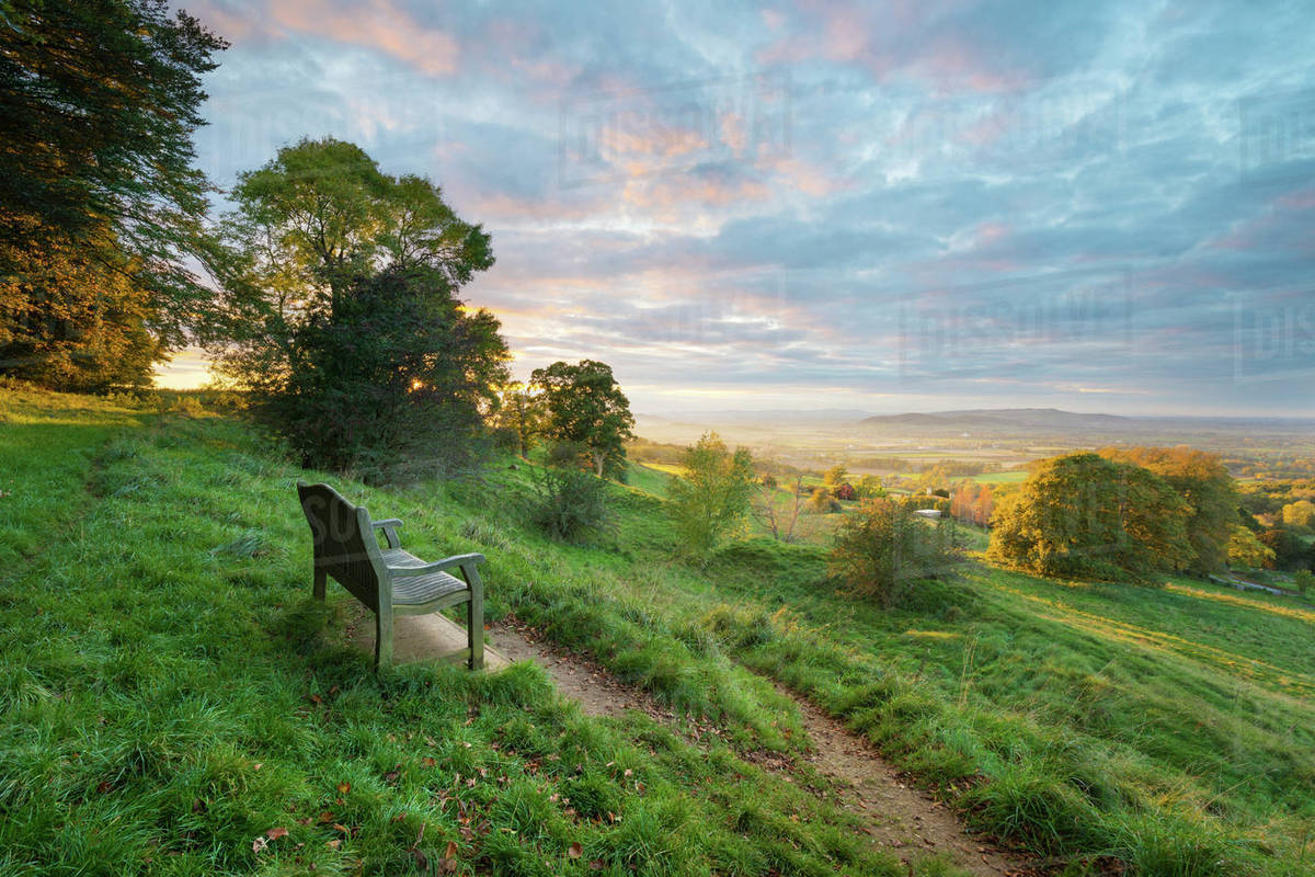 Cotswold Way path and bench with views to the Malvern Hills at sunset