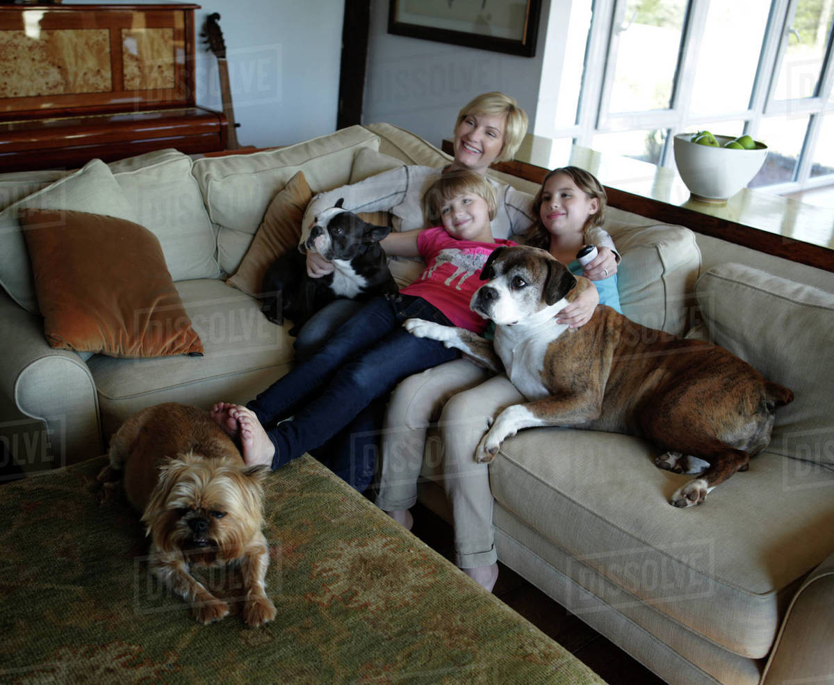 Mother and daughters sitting on sofa with pets dogs, watching TV together Royalty-free stock photo