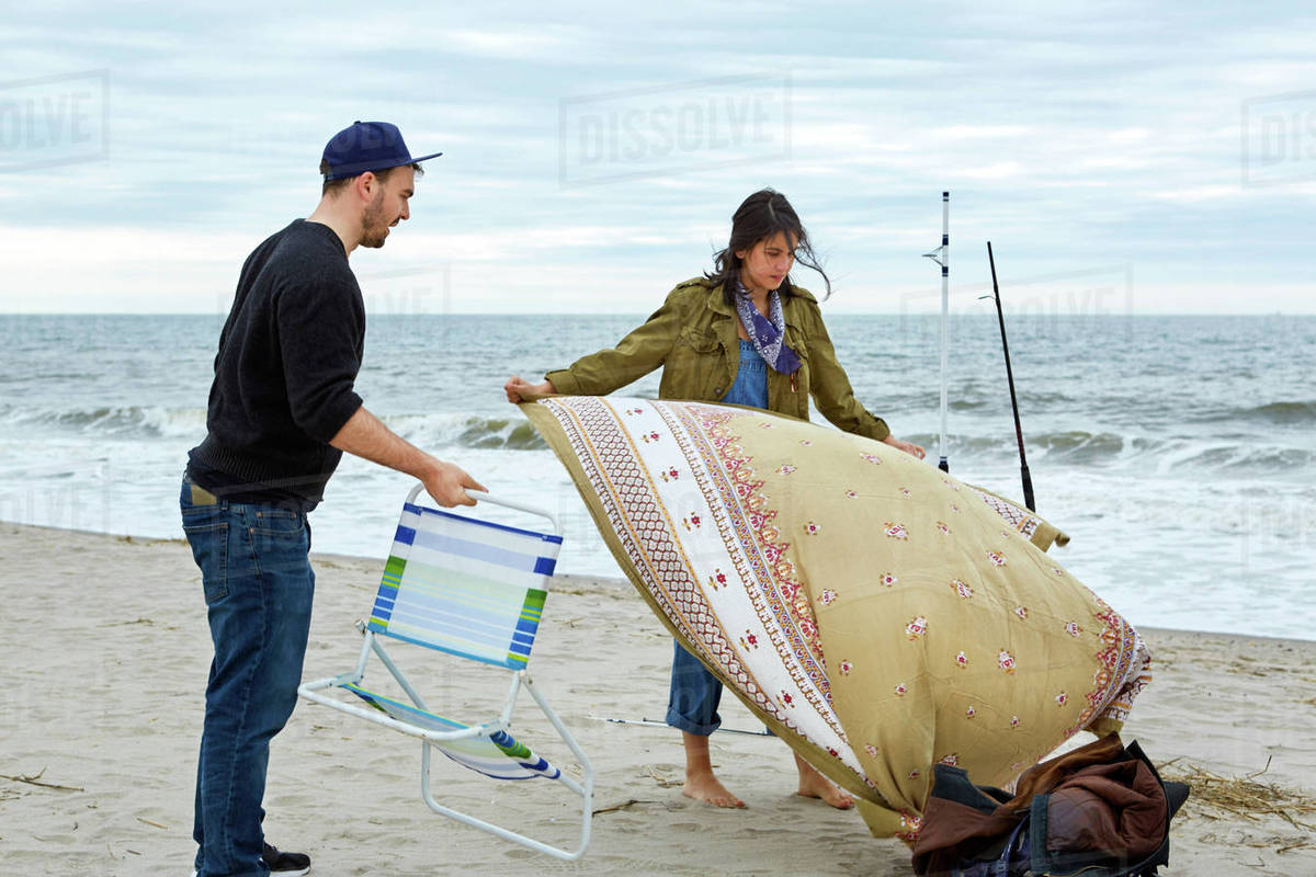 Young Sea Fishing Couple Preparing Beach Chair And Picnic Blanket On Young Sea Fishing Couple Preparing Beach Chair And Picnic Blanket On
