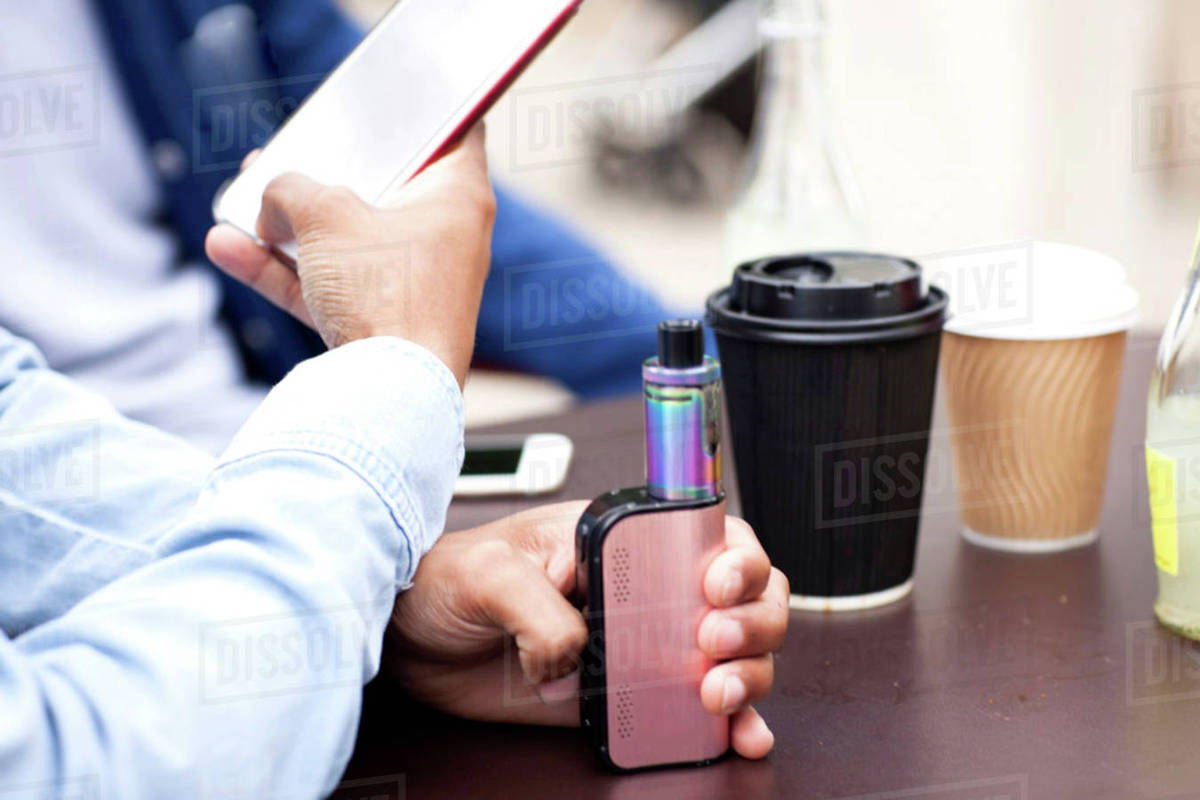 cropped view of man holding smartphone and vape stock photo dissolve