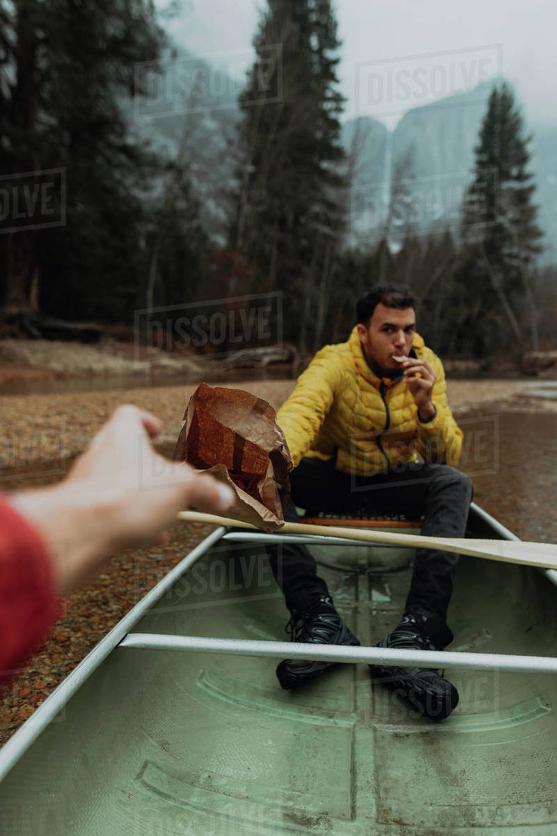 Young canoeing couple sharing snacks on canoe, personal perspective, Yosemite Village