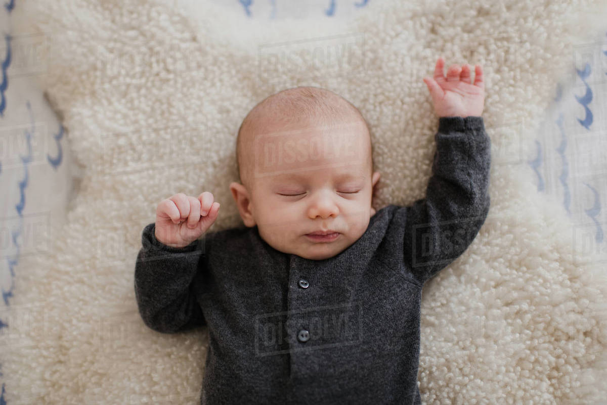 Baby boy sleeping on sheepskin rug in crib, overhead view Stock Photo