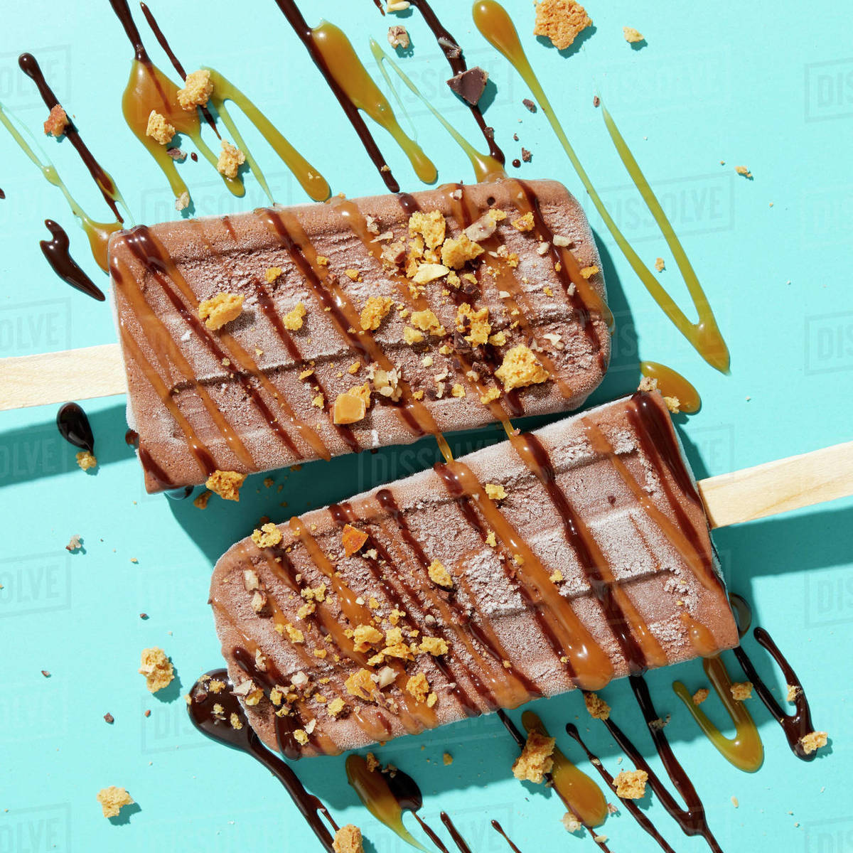 Two homemade fudge iced lollies with sprinkled and drizzled nuts