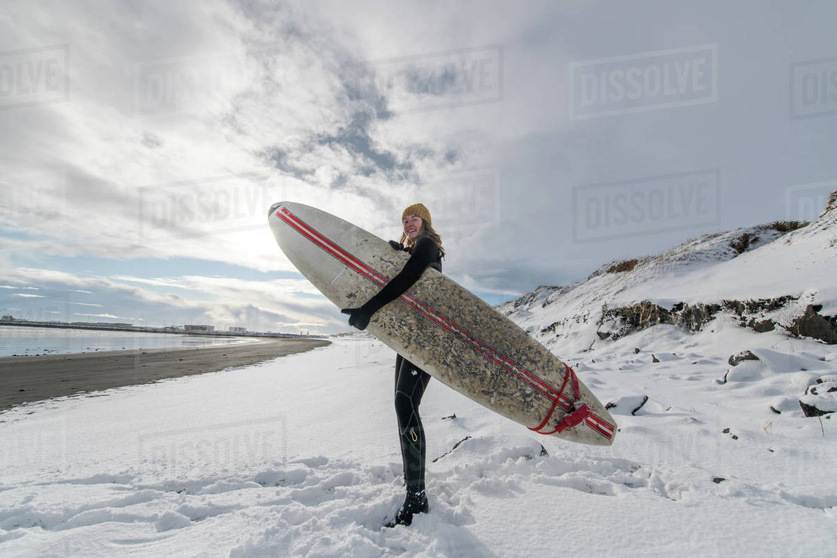 A woman wearing a wetsuit and holding a surfboard standing on a snowy
