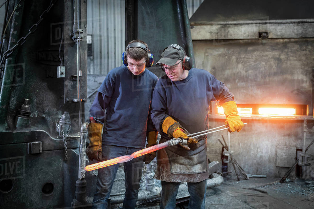 Engineer with apprentice inspecting a steel part in industrial
