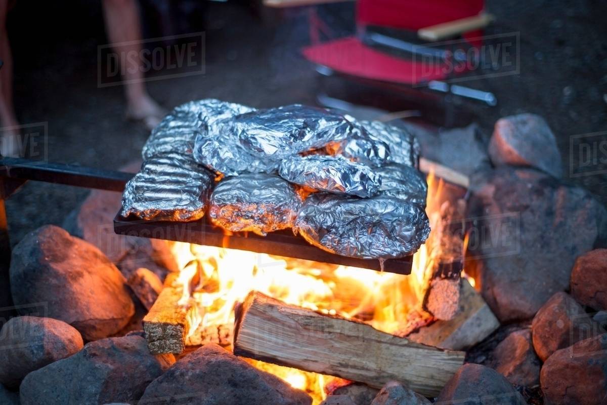 Food wrapped in tin foil cooking over campfire Stock Photo Dissolve