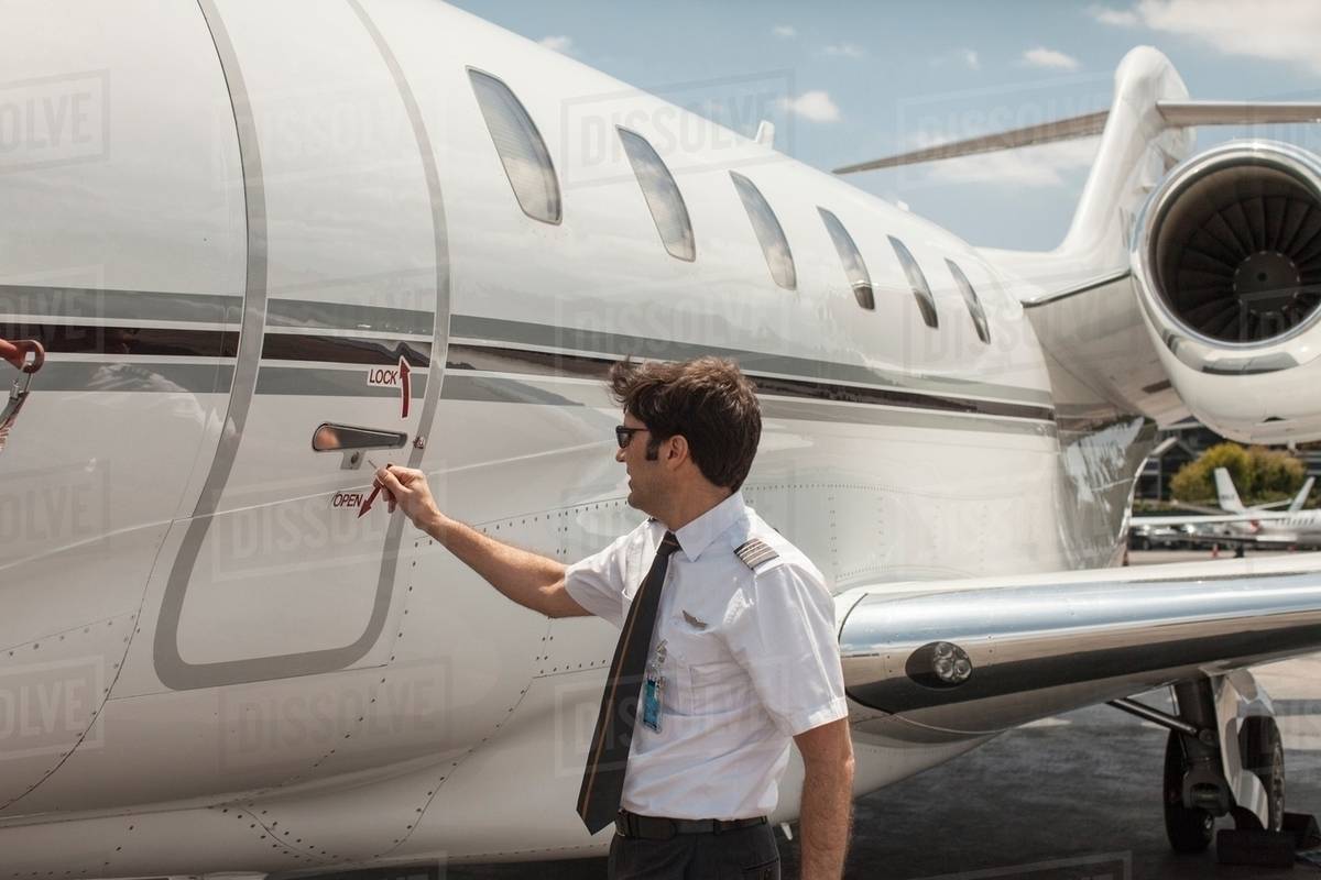 Male private jet pilot locking plane door at airport Stock Photo