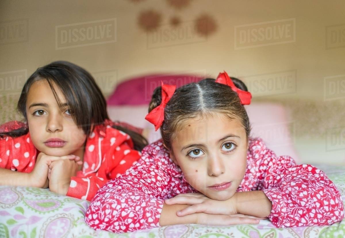 Portrait of two sisters lying on bed gazing Stock Photo Dissolve