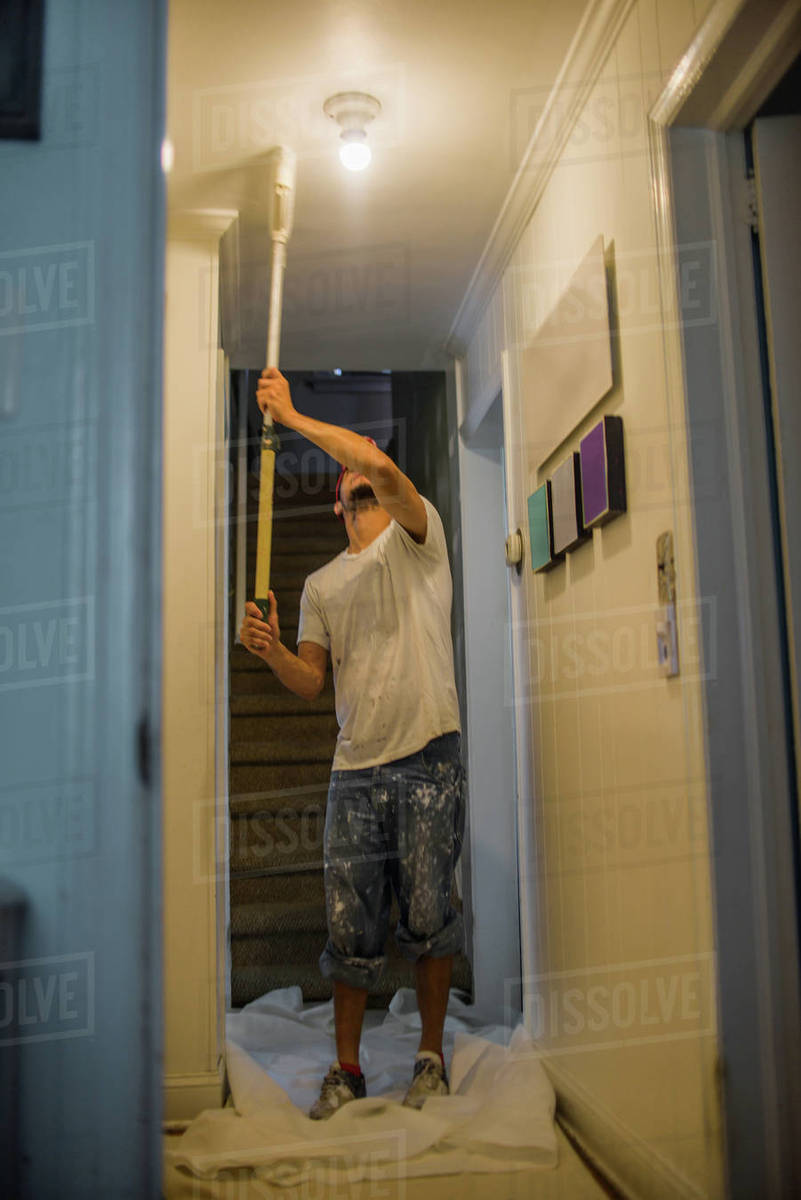 Man Painting Passage Ceiling With Paint Roller Stock Photo
