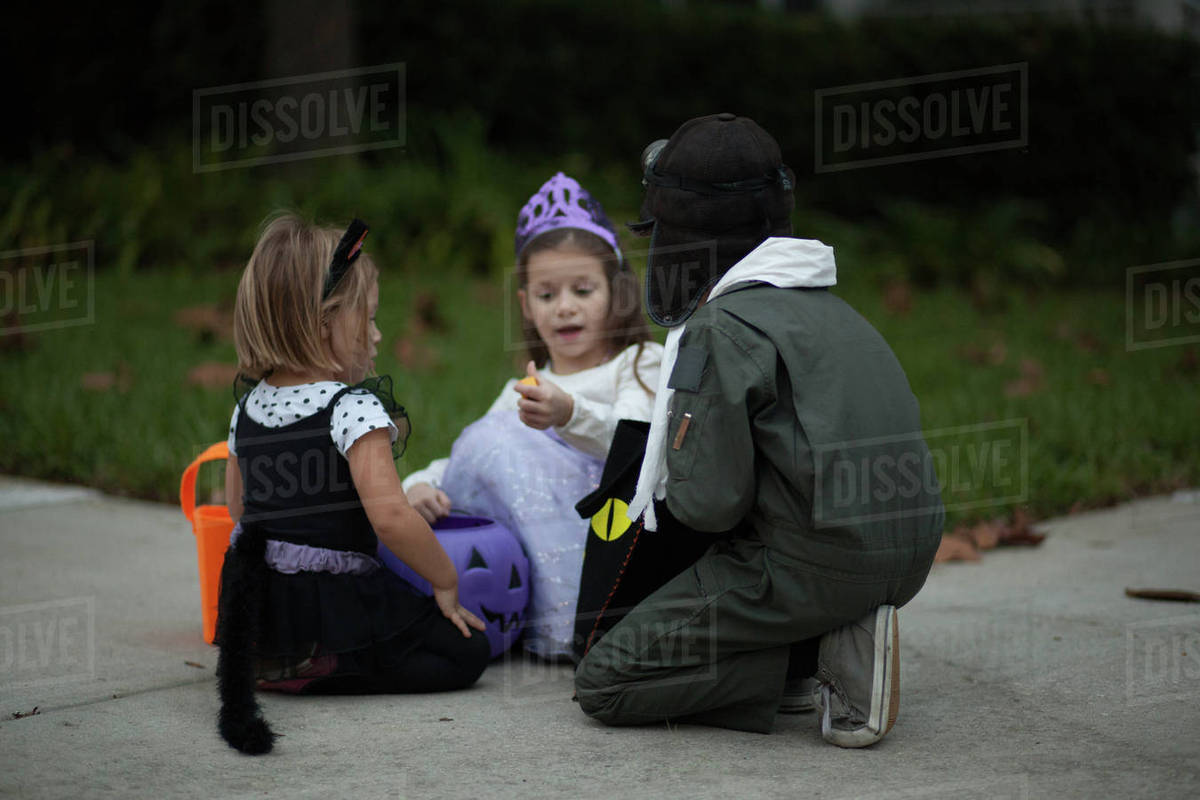 Boy and sisters trick or treating crouching and looking at treats on sidewalk Royalty-free stock photo