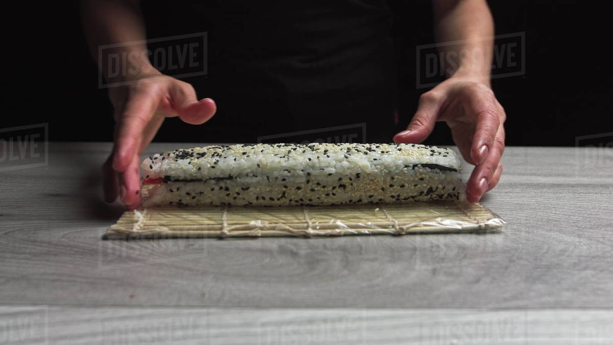 Chef in gloves is cooking sushi maki using mat. Maki are made of rice