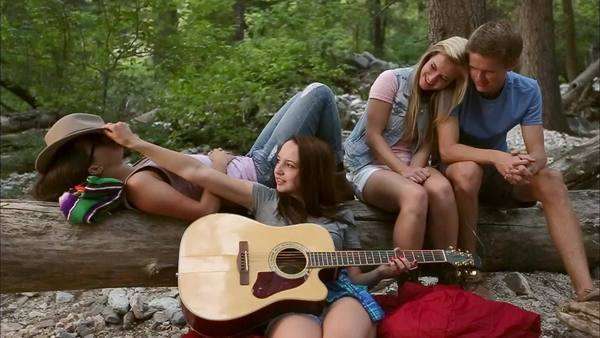 2 girls lay on a log their friend plays guitar and they laugh