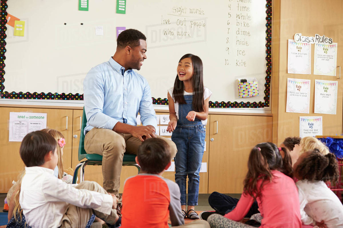 Schoolgirl At Front Of Elementary Class Talking With Teacher Schoolgirl At Front Of Elementary Class Talking With Teacher