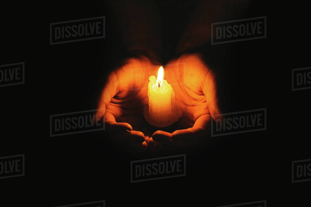 A hand holding igniting candle with black background for memories