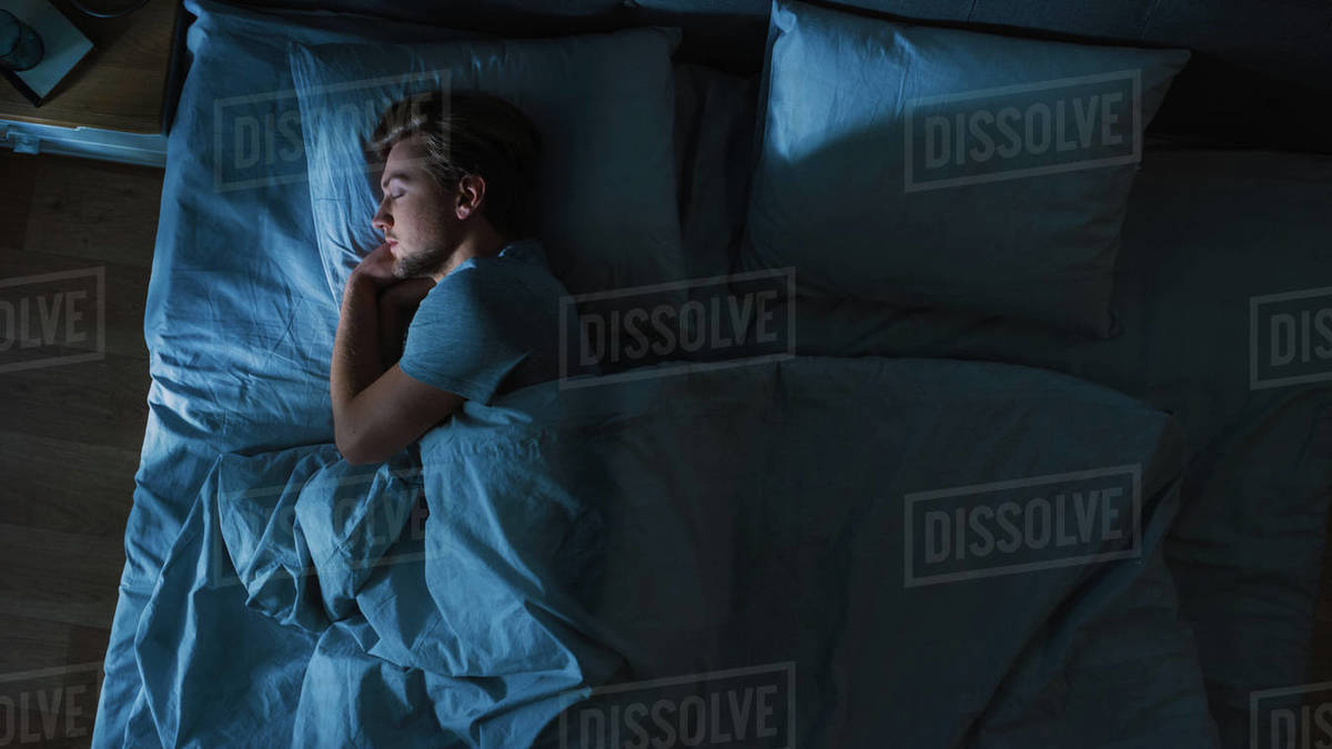 Top View of Handsome Young Man Sleeping Cozily on a Bed in His Bedroom