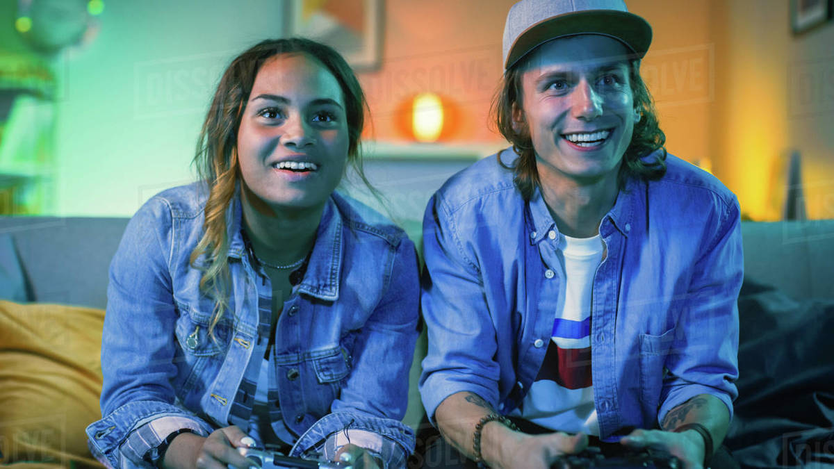 Excited black gamer girl and young man sitting on a couch and playing ...