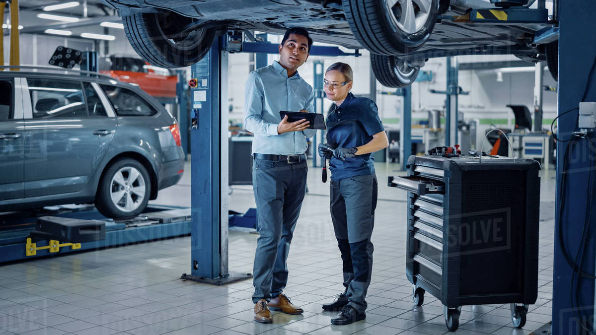 Female Mechanic Talking to a Manager Under a Vehicle in a Car Service