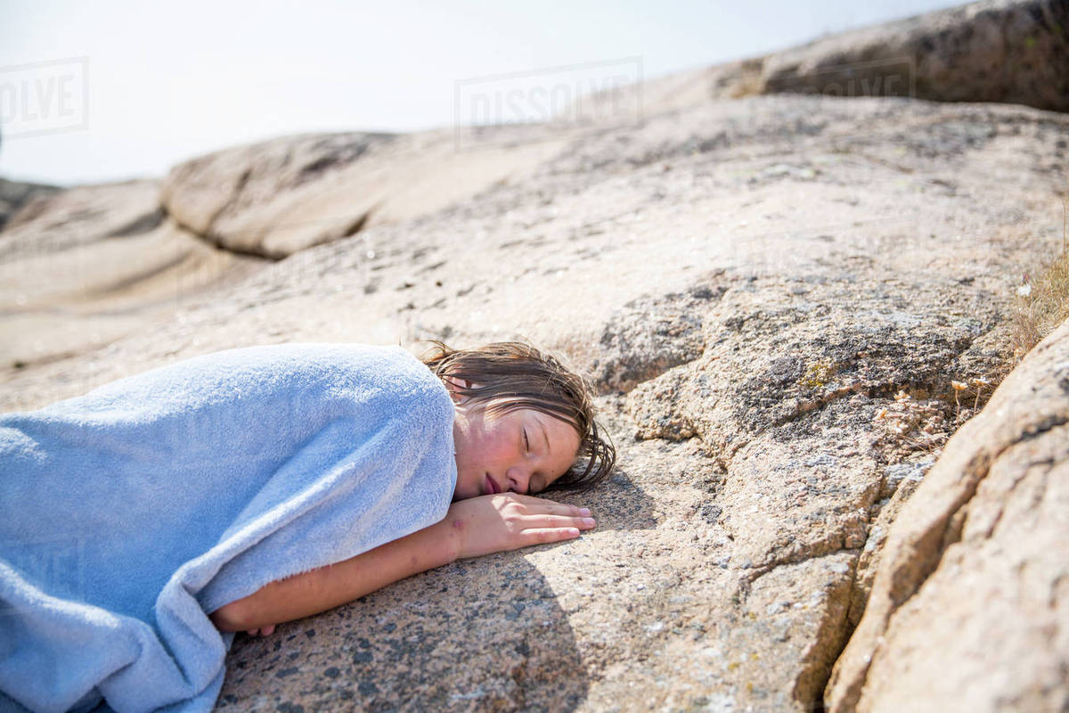 Boy covered with blanket sleeping on rock Stock Photo Dissolve