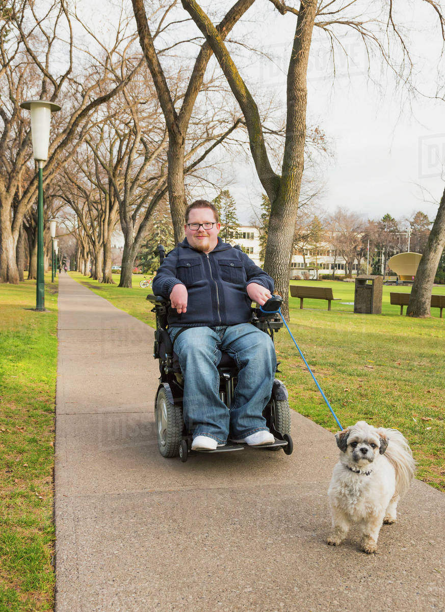 Disabled man using his powered wheelchair and walking his dog in a park in autumn; Edmonton