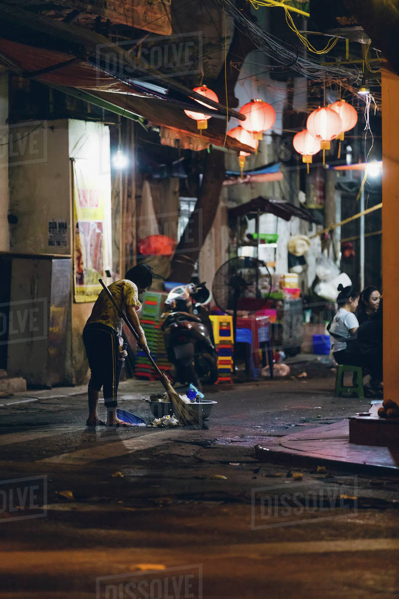 Woman sweeping up garbage in the street at night; Hanoi, Veitnam