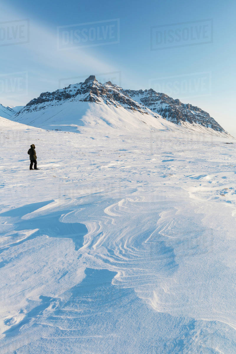 Man in a parka standing on the windswept snow, sastrugi patterns in the
