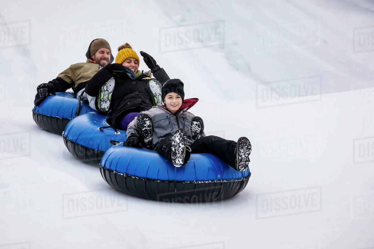 A group of scared family members tubing down a ski hill together in tandem; Fairmont Hot Springs