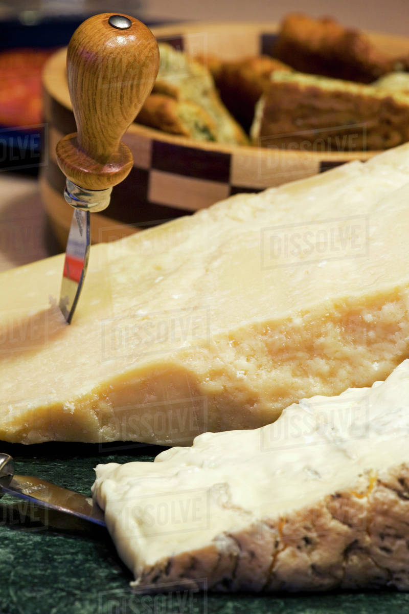 A block of parmesan and cheese with knives and wooden bowl