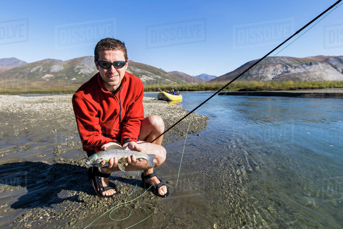 A fisherman holds a fresh grayling fish caught by fly A fisherman holds a fresh grayling fish caught by fly