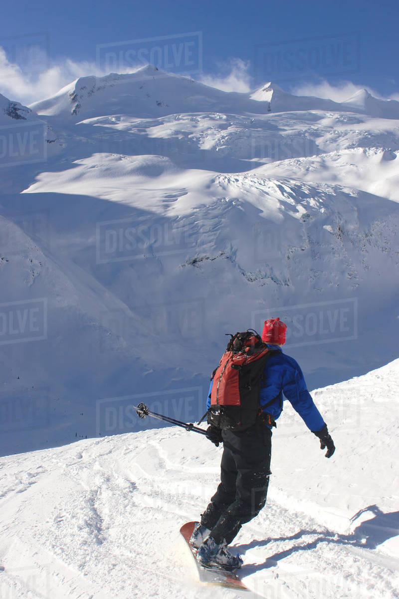 A back country snowboarder descends a snow field toward a glacier.; Selkirk Mountains, British Columbia, Canada. Royalty-free stock photo