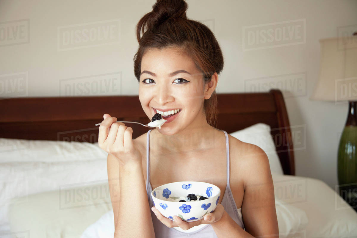 A girl sitting on her bed eating a snack from a bowl;Berkeley