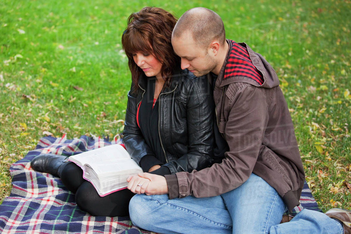 Couple Reading Bible And Praying Together In The Park; Edmonton, Alberta, Canada Stock Photo