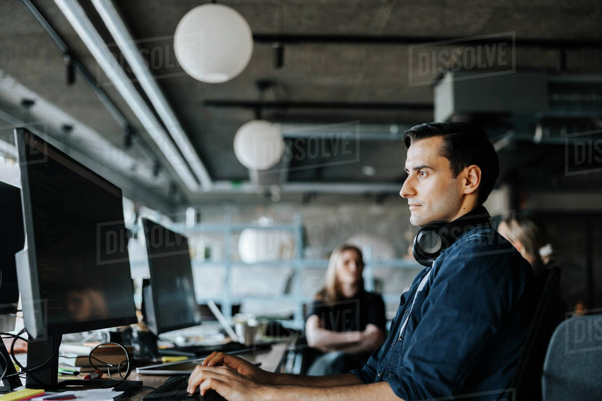 Side view of male tech programmer with headphones coding at office ...