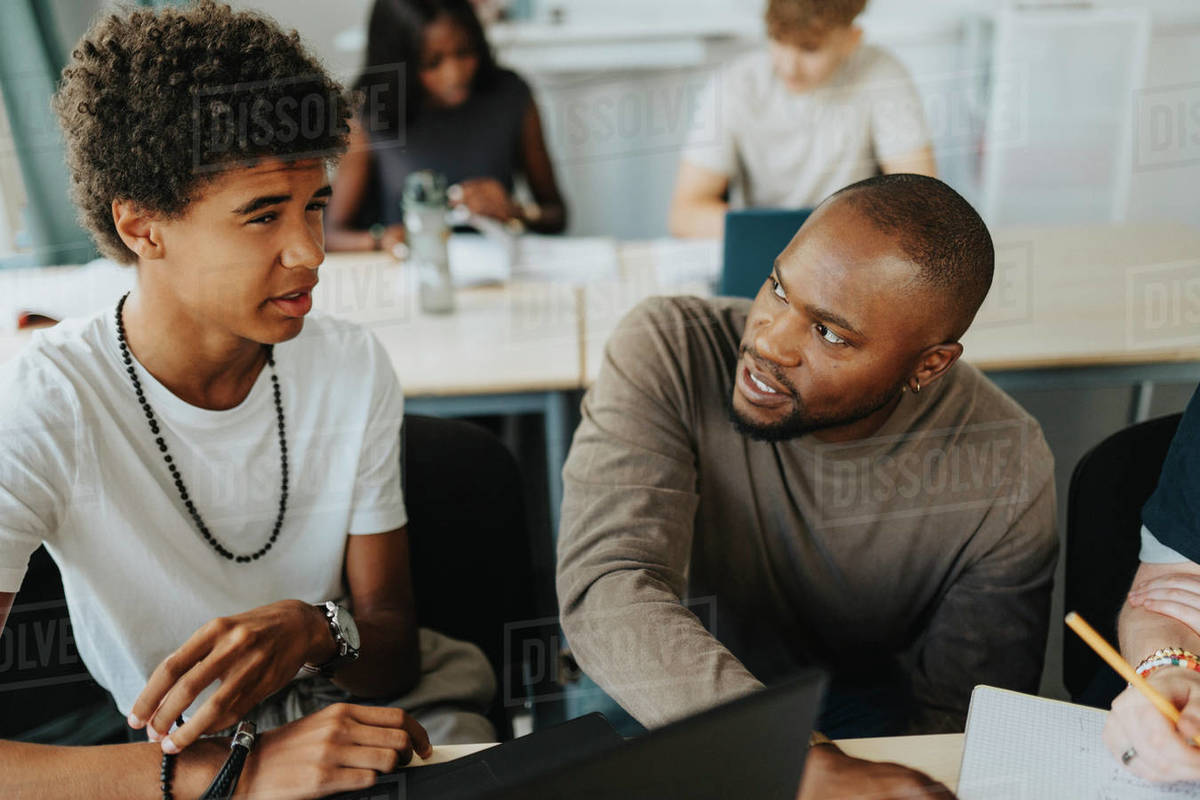 Teenage male student discussing with teacher in classroom at high ...