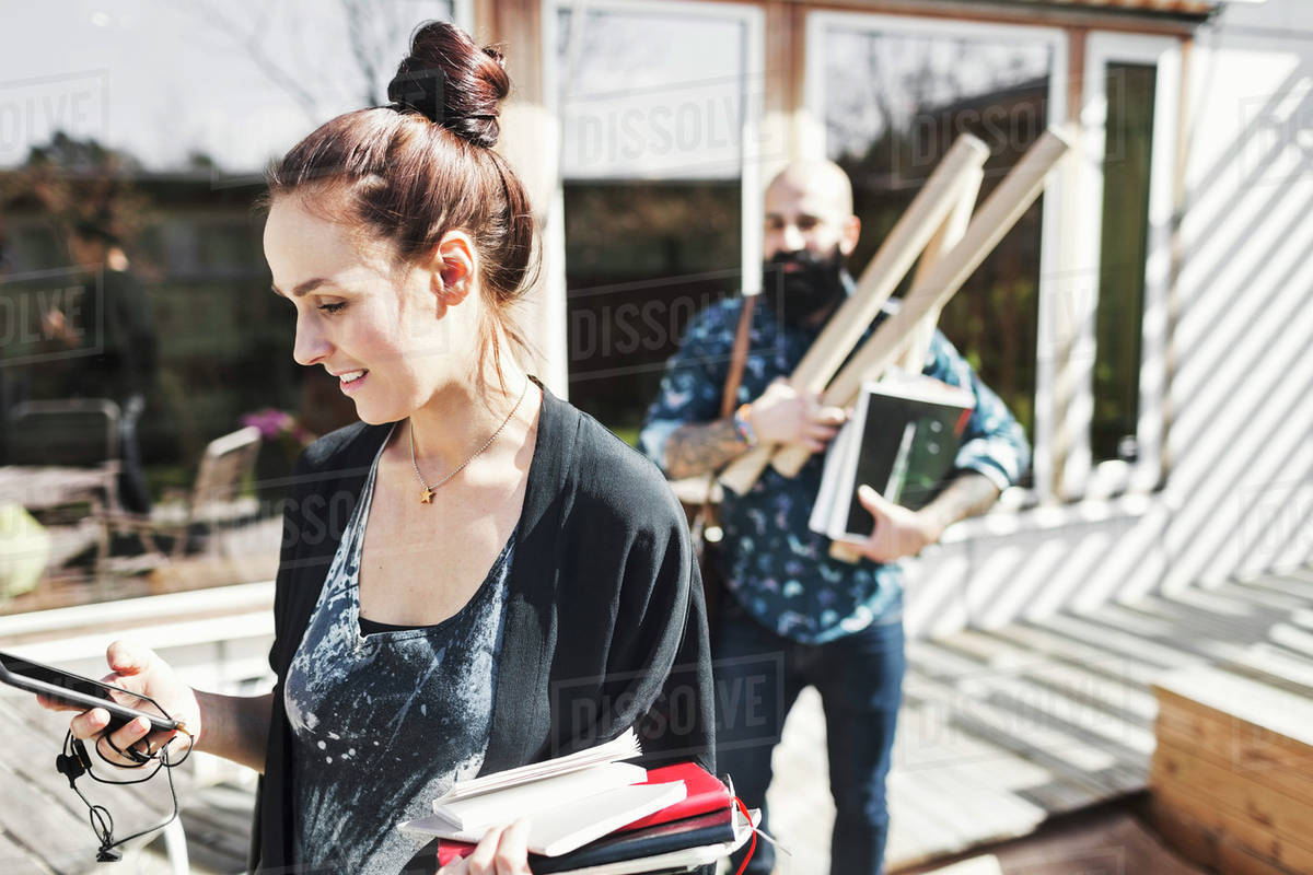 Smiling architect using mobile phone while colleague holding blueprints in background at yard Royalty-free stock photo