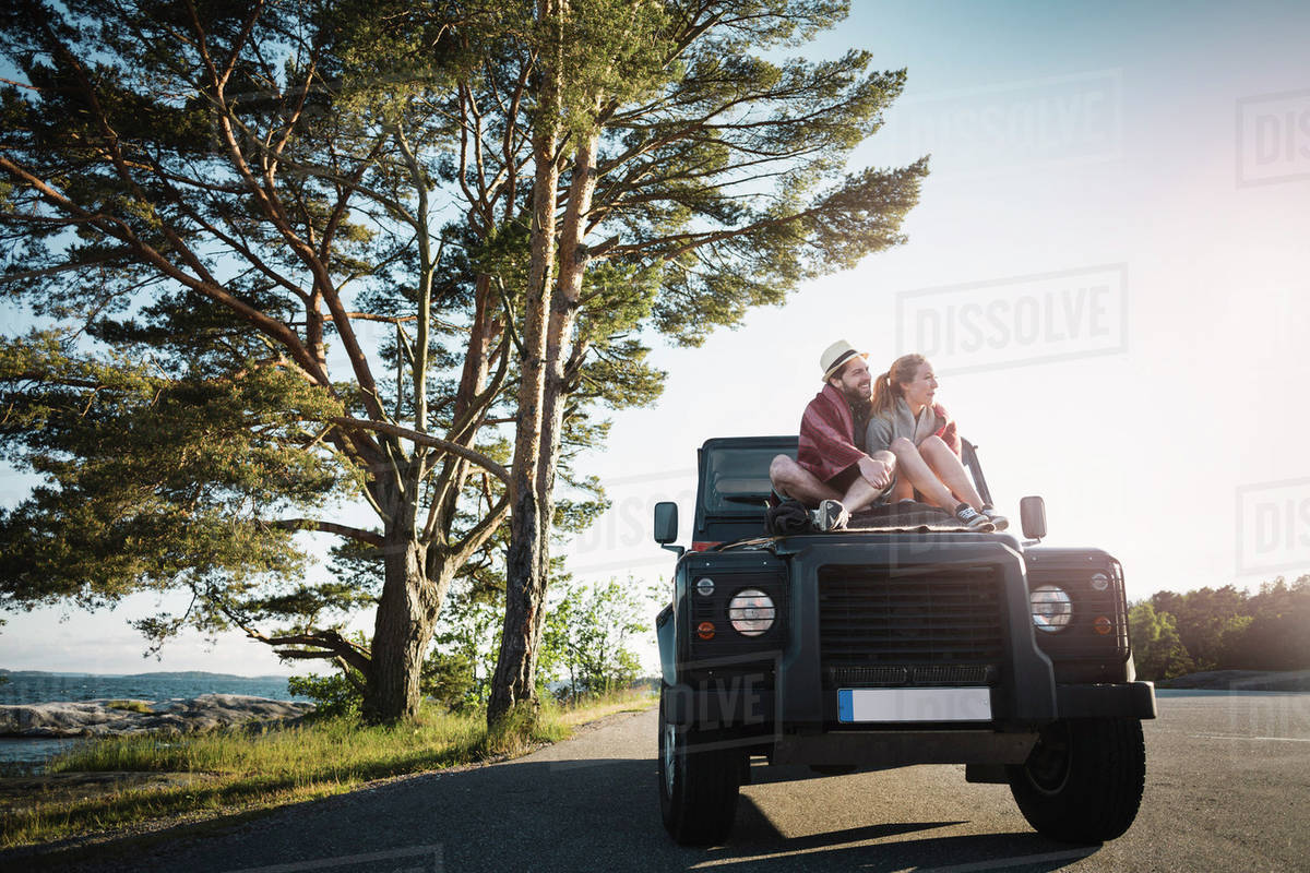 Couple sitting on jeep at countryside Stock Photo Dissolve