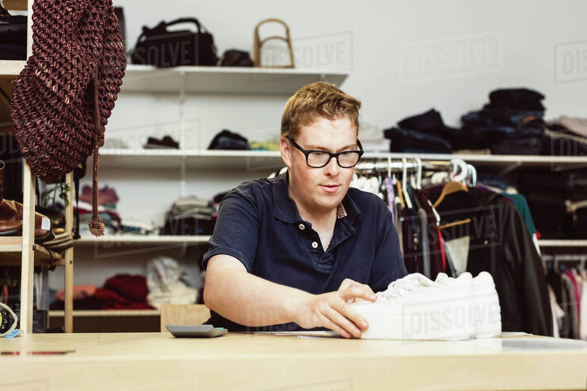 Cashier holding shoes on table while calculating in clothing store